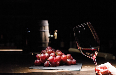 Woman holds glass of wine before bunch of grape lying on black plate
